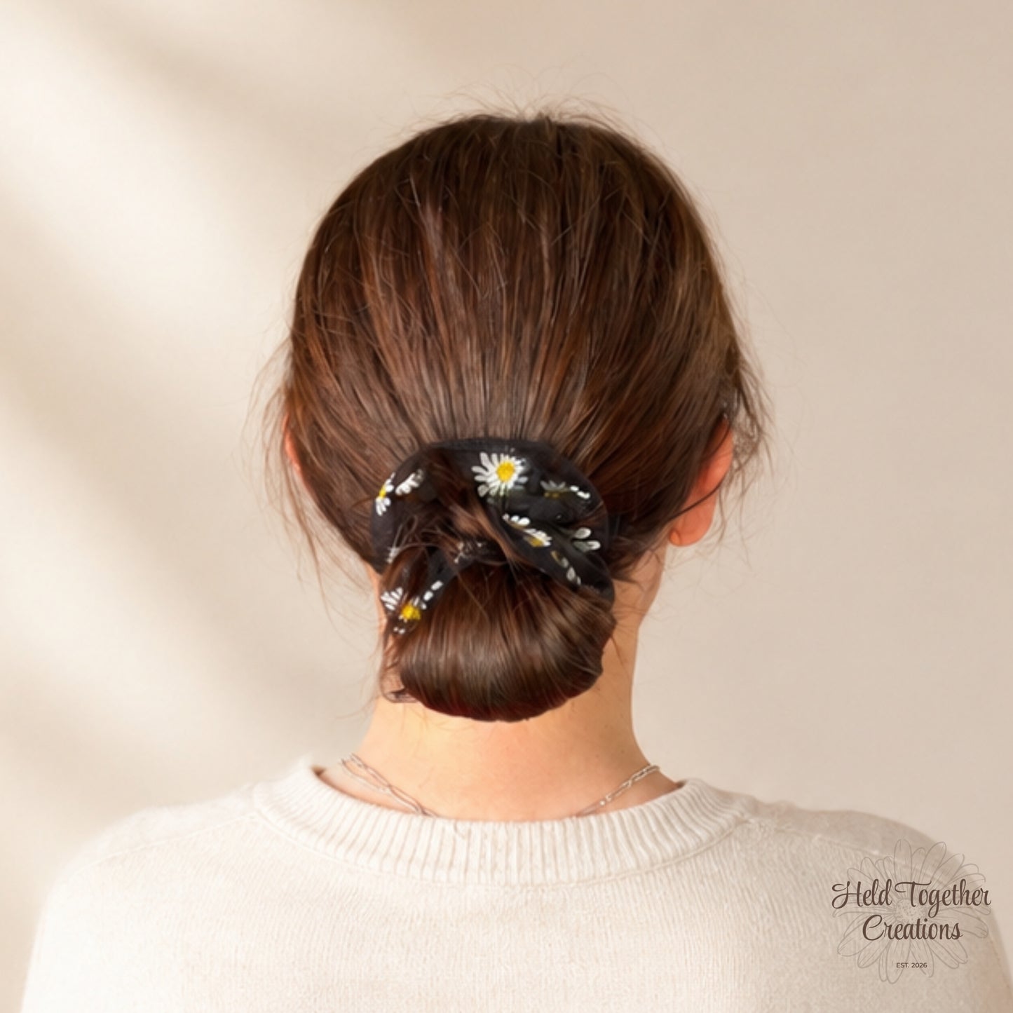 Black daisy puff scrunchie worn around a low bun hairstyle