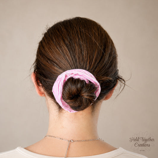 Person with a pink scrunchie in their hair against a neutral background