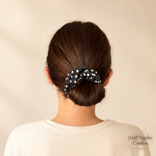 Person with a bun holding a black polka dot scrunchie against a beige background