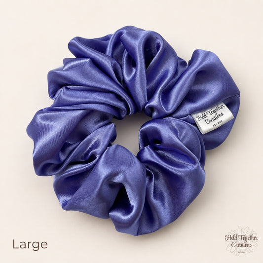 Large lilac satin scrunchie laid flat showing glossy gathered fabric and brand tag.