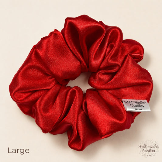 Large red satin scrunchie on warm ivory background with branded tag