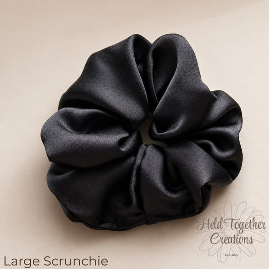 Midnight Gloss black satin scrunchies in large and small sizes styled on a soft neutral background.