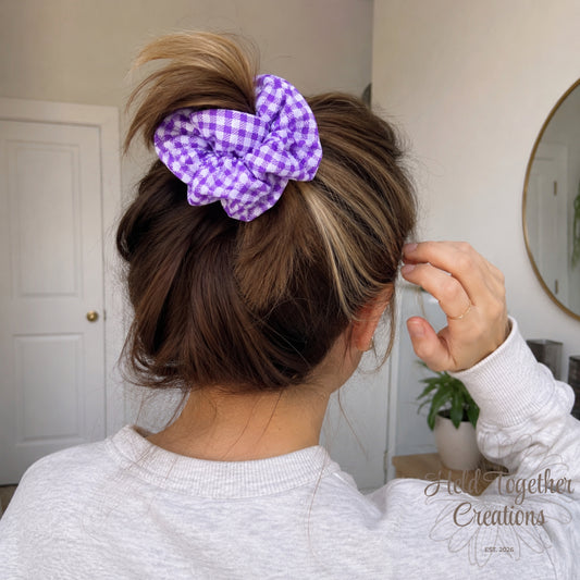 Person adjusting a purple scrunchie in their hair with a neutral background