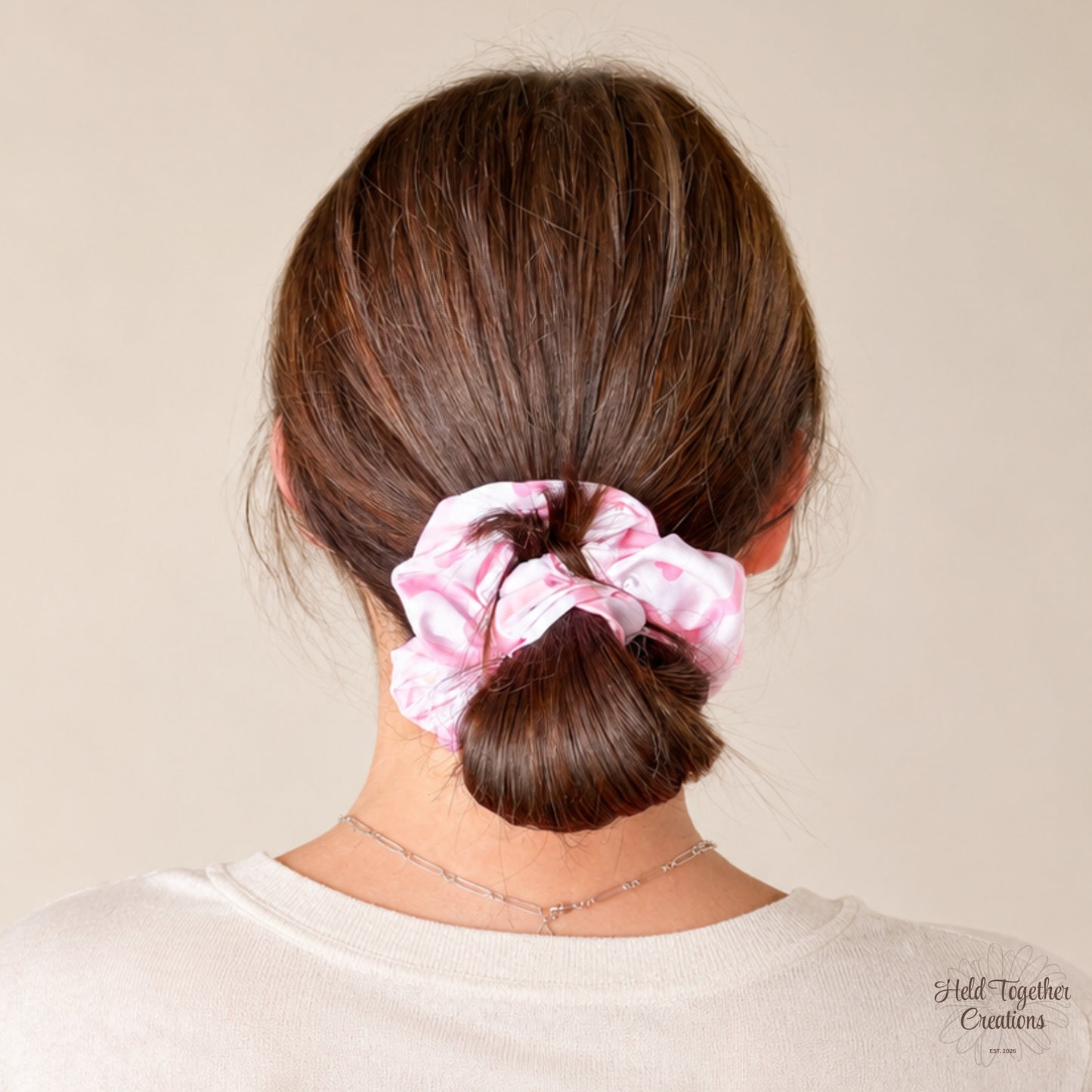 A person shown from the back wearing a light pink and white patterned fabric scrunchie in their brown hair, against a plain beige background.