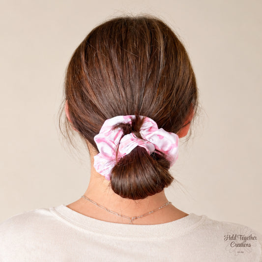 A person shown from the back wearing a light pink and white patterned fabric scrunchie in their brown hair, against a plain beige background.