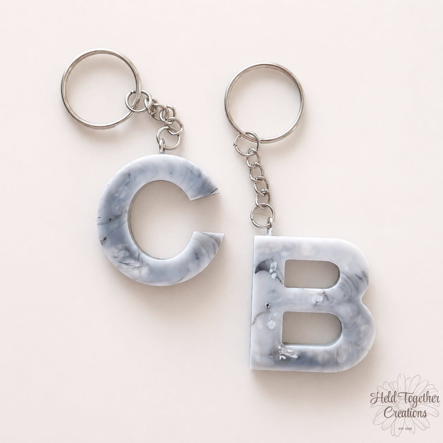 Marble-textured 'C' and 'B' keychains on a light pink background