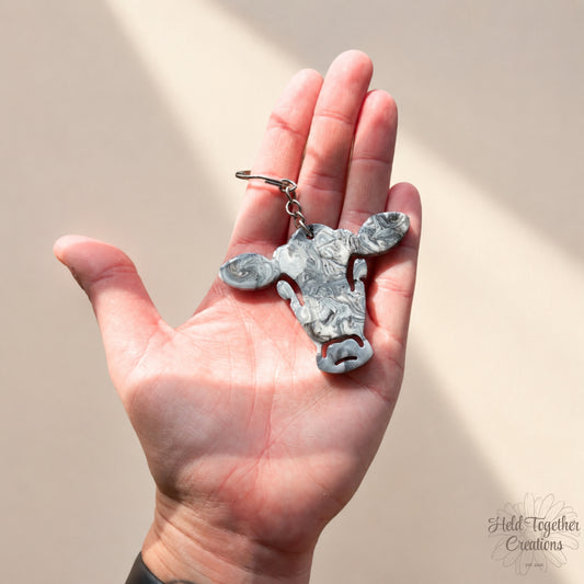 Handmade black, white and grey marble resin cow keyring with silver hardware on a soft neutral background.