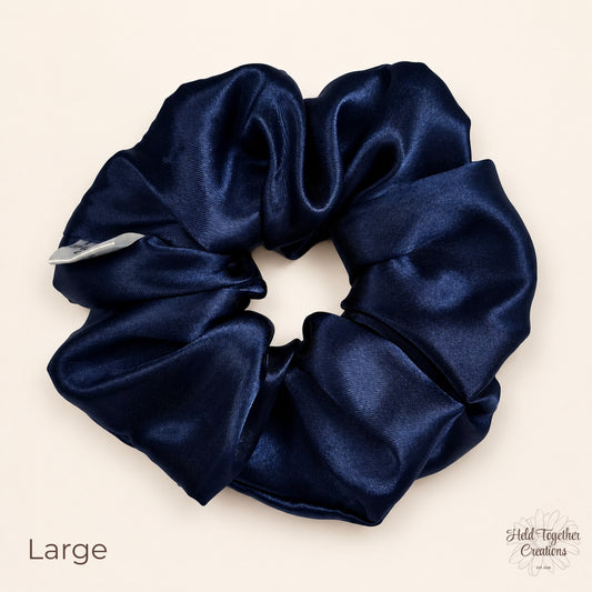 Navy satin scrunchie on a warm ivory background showing glossy fabric folds and Held Together Creations label.