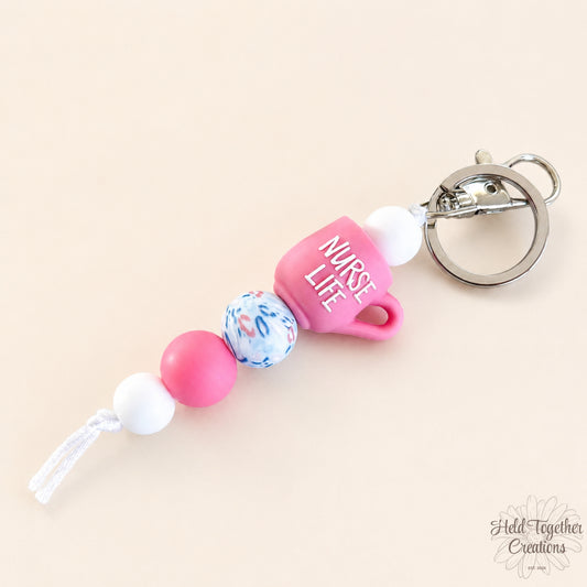 Handmade nurse life silicone bead keyrings with pink, teal and white silicone beads, medical charms and silver keyring hardware on a soft neutral background.