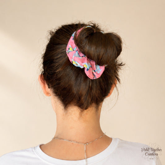 Party Pup Scrunchie worn around a messy bun, featuring colourful cartoon pups on bright pink fabric.