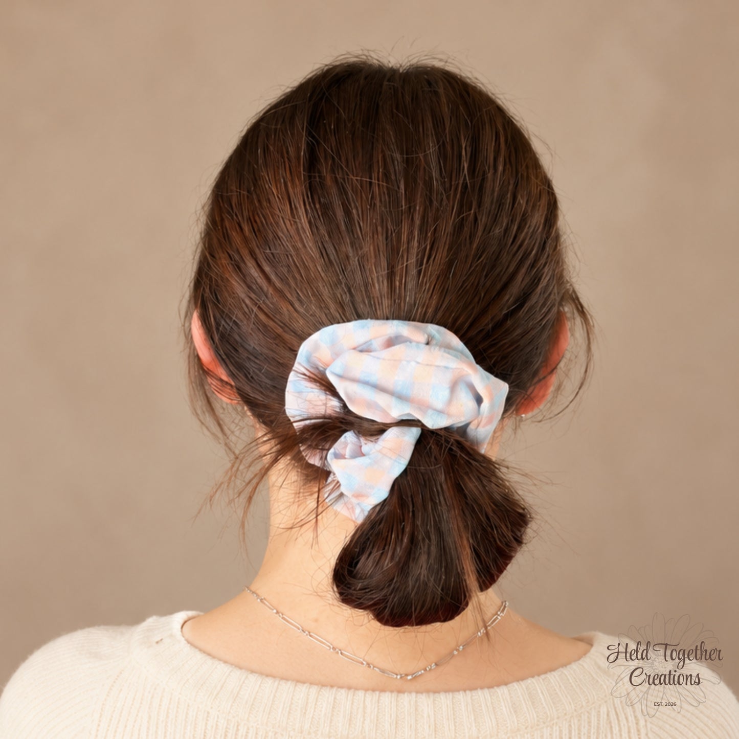 Pastel Picnic handmade fabric scrunchie with a soft pink and blue check pattern on a warm neutral background.