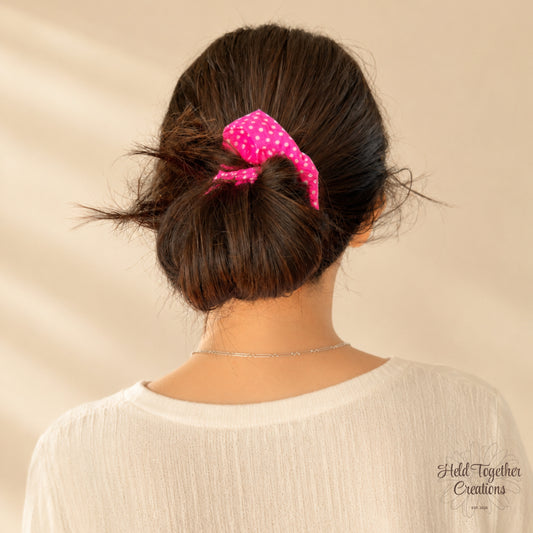 Person with a bun holding a pink scrunchie against a beige background