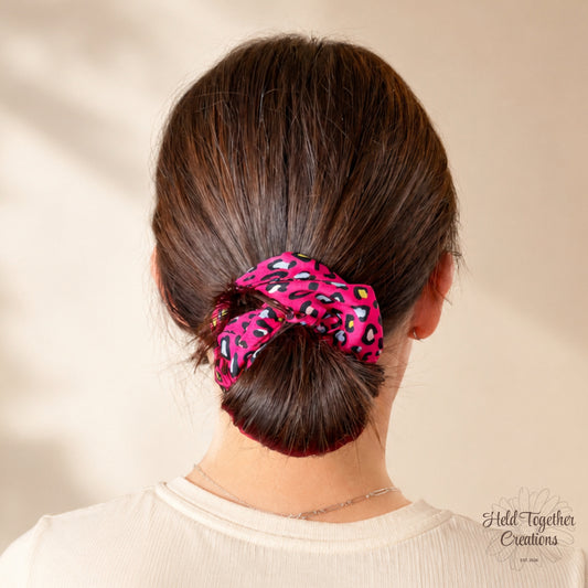 Pink leopard print scrunchie worn around a low bun hairstyle.