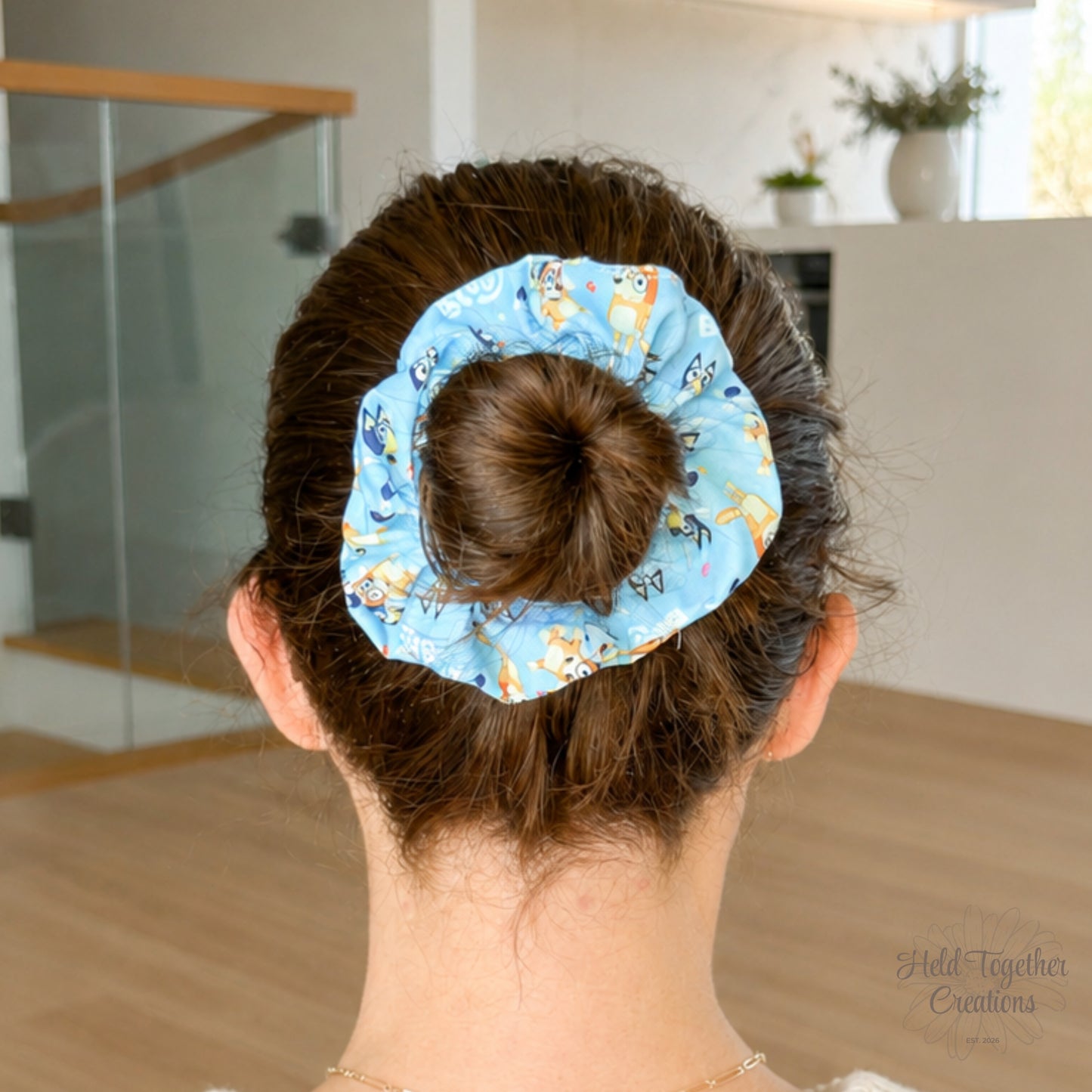 Playdate Blue scrunchie styled in a brown hair bun, showing the blue puppy-print fabric in a bright home setting.