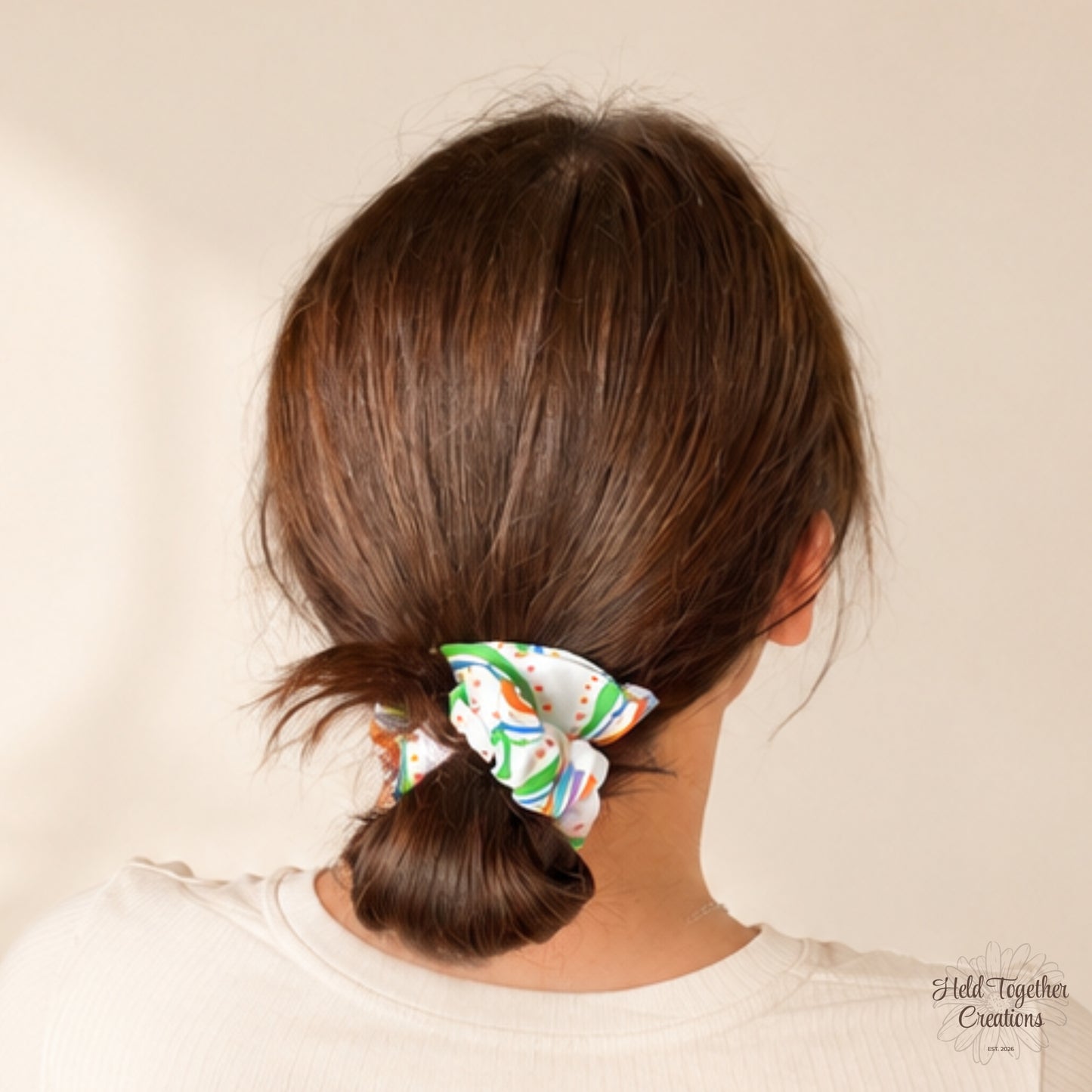 Rainbow Rush Scrunchie styled in a low bun, showing colourful rainbow print on white fabric.