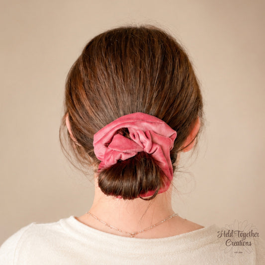Pink velvet handmade scrunchie on a warm ivory background.