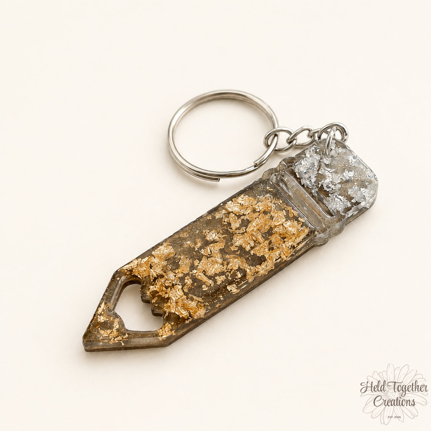 Handmade pencil-shaped resin keyring with gold and silver flakes and metal keyring hardware on a soft neutral background.