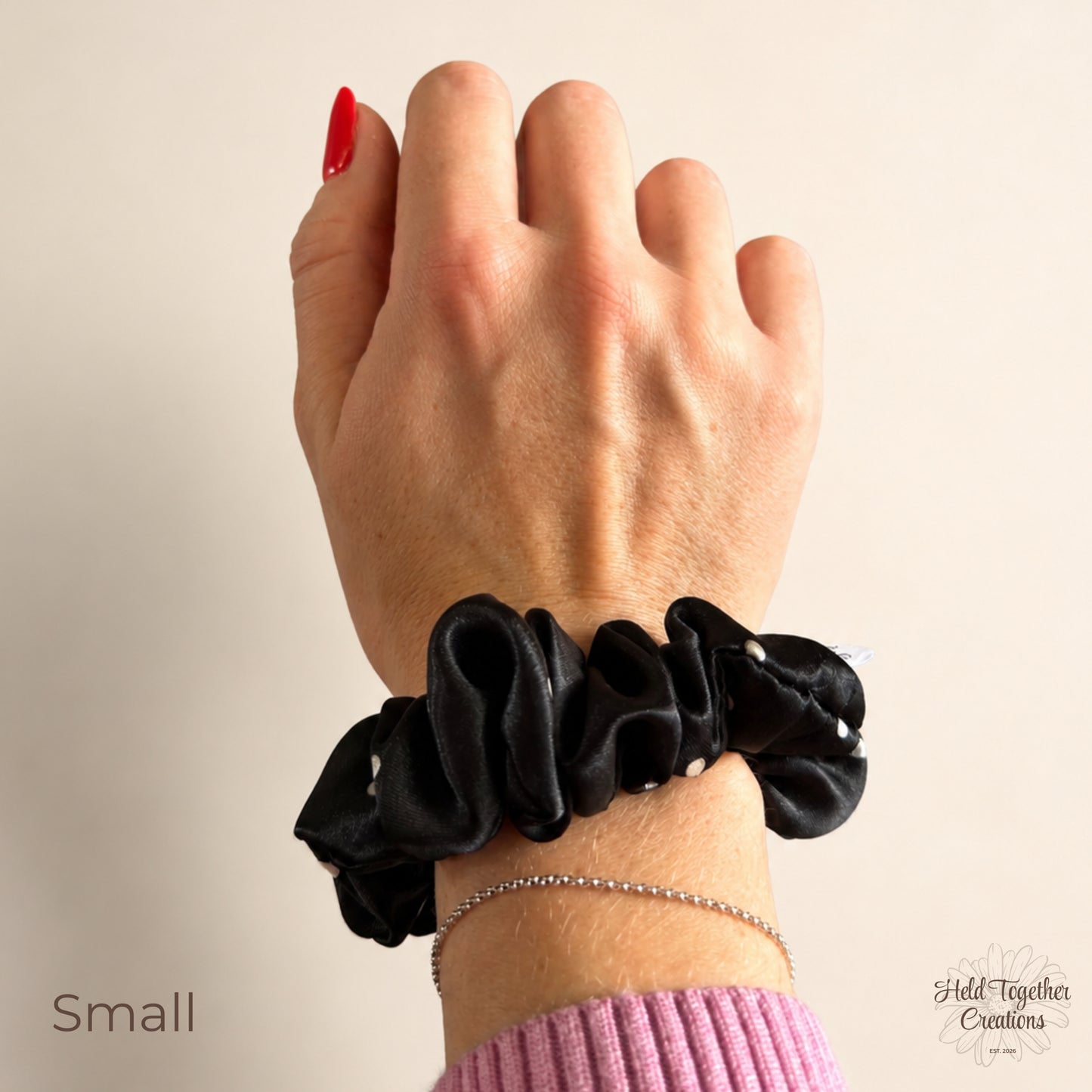 Small black satin scrunchie with white spots worn on the wrist, showing its compact gathered style.