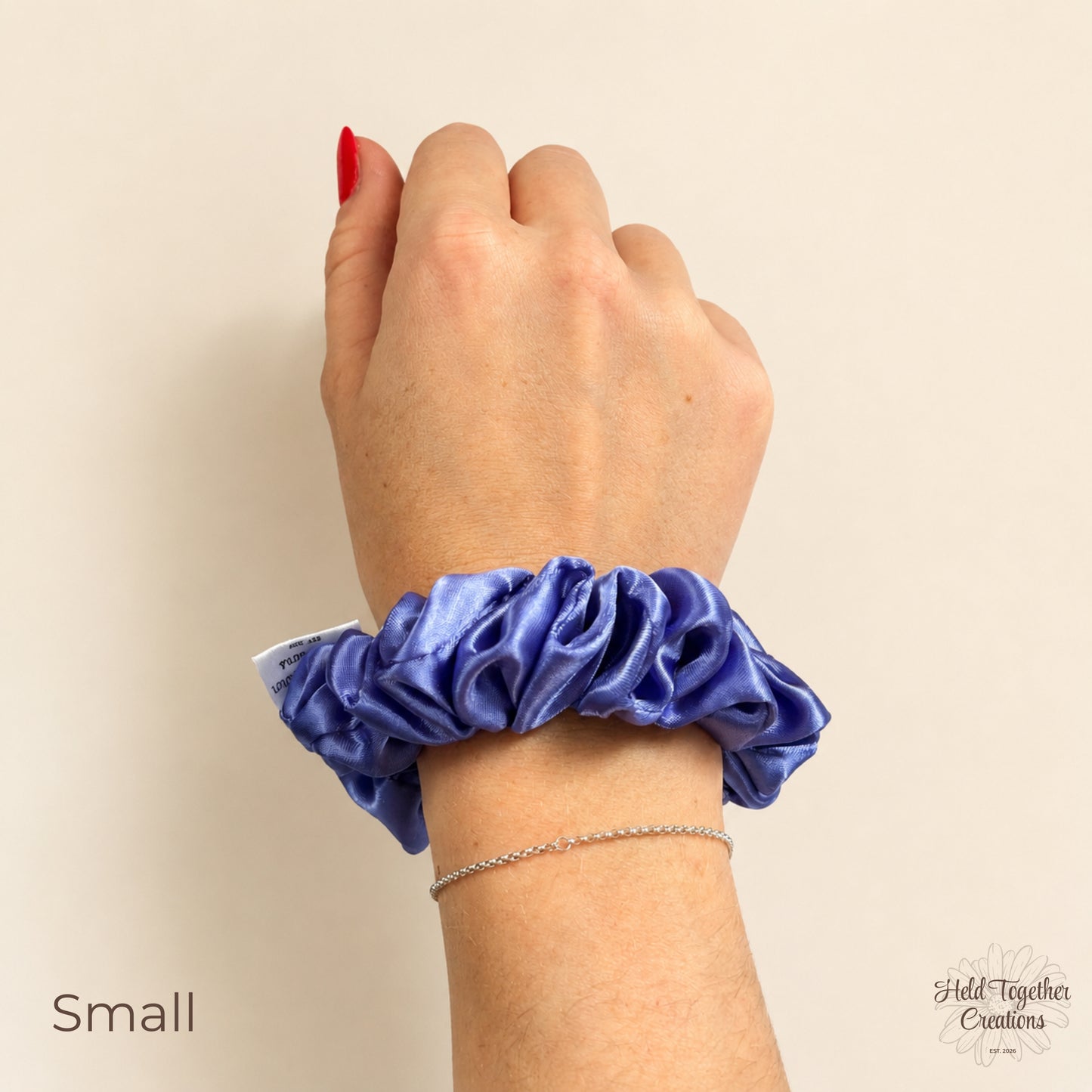 Small lilac satin scrunchie worn on wrist against a warm ivory background.