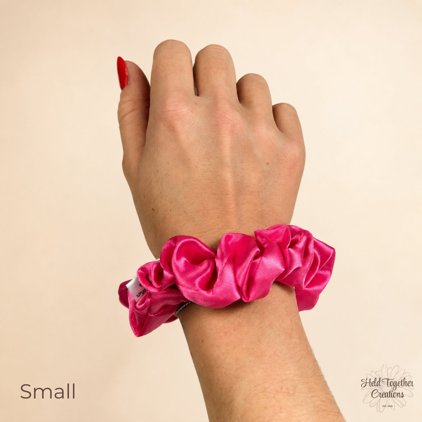 Small pink satin scrunchie worn on wrist against a warm ivory background.