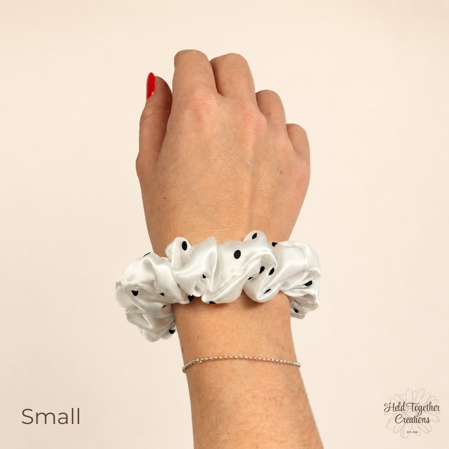 Small white satin scrunchie with black polka dots worn on wrist.