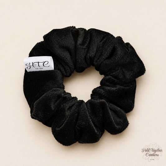 Black velvet handmade scrunchie with white HTC label on a warm neutral background.