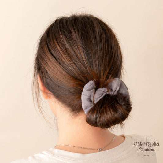 Handmade Storm Linen Scrunchie in textured grey-purple fabric on a warm ivory background.
