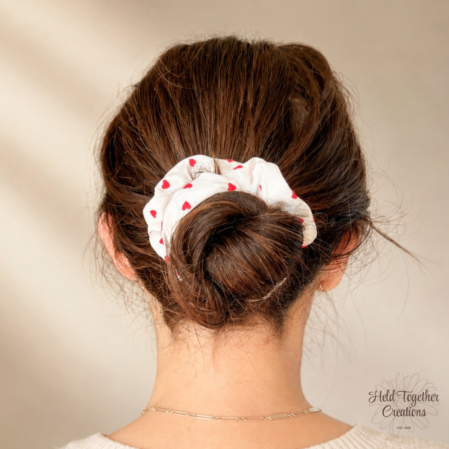 White velvet-style scrunchie with red heart print on a warm ivory background.