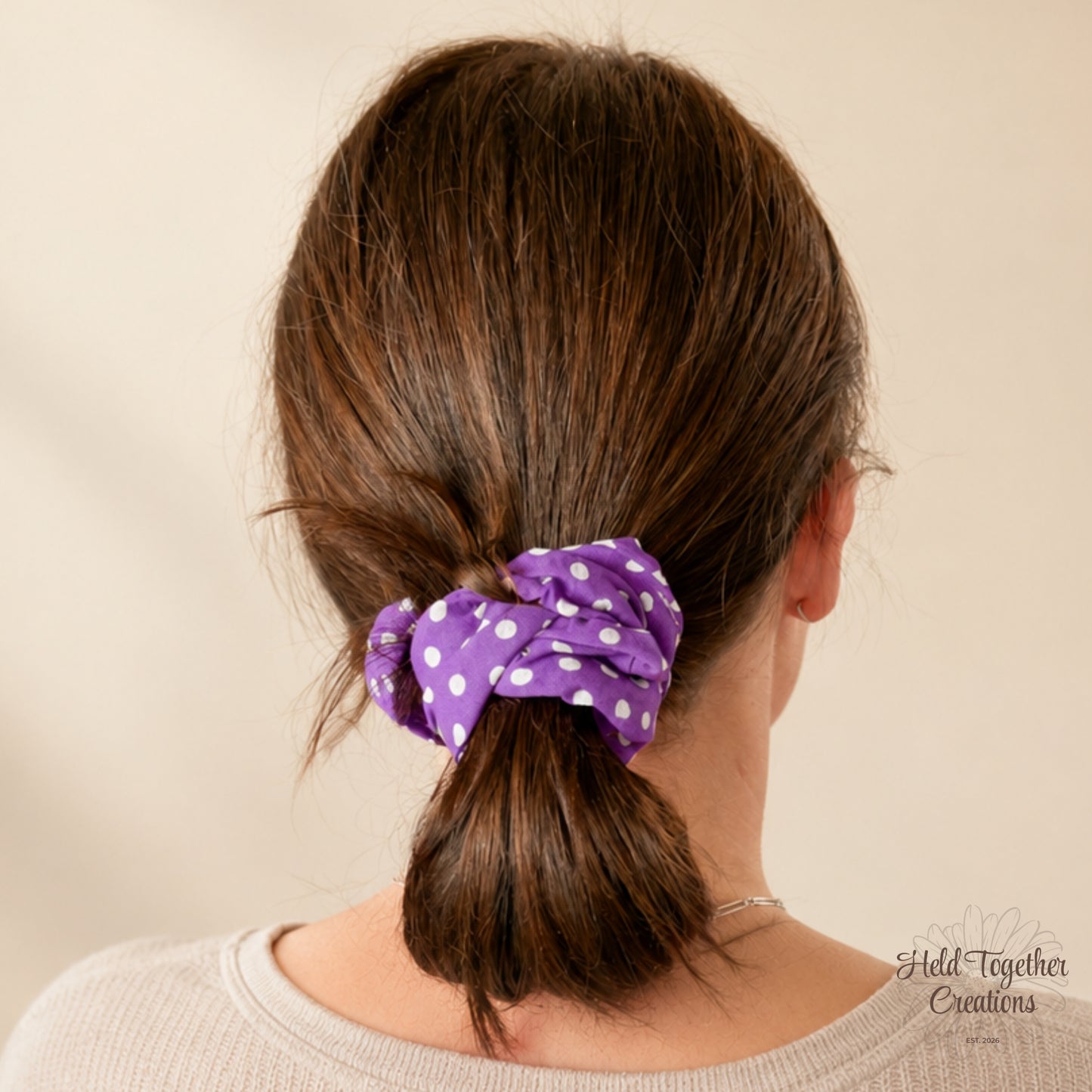 Person with brown hair tied into a ponytail with a purple scrunchie, on a beige background.