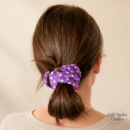 Person with brown hair tied into a ponytail with a purple scrunchie, on a beige background.