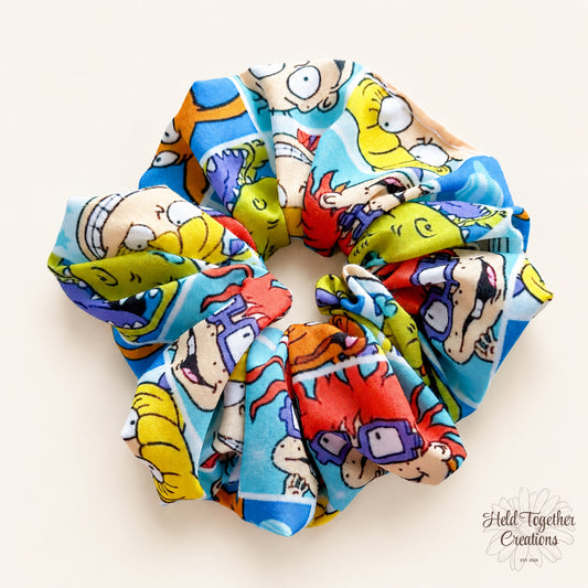 Colourful 90s Chaos handmade scrunchie with bright retro cartoon-style print on a warm ivory background.