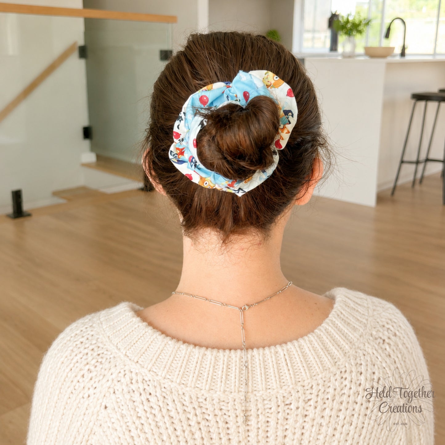 Balloon Bash scrunchie styled in a brown hair bun, showing the blue puppy-print fabric in a bright home setting.
