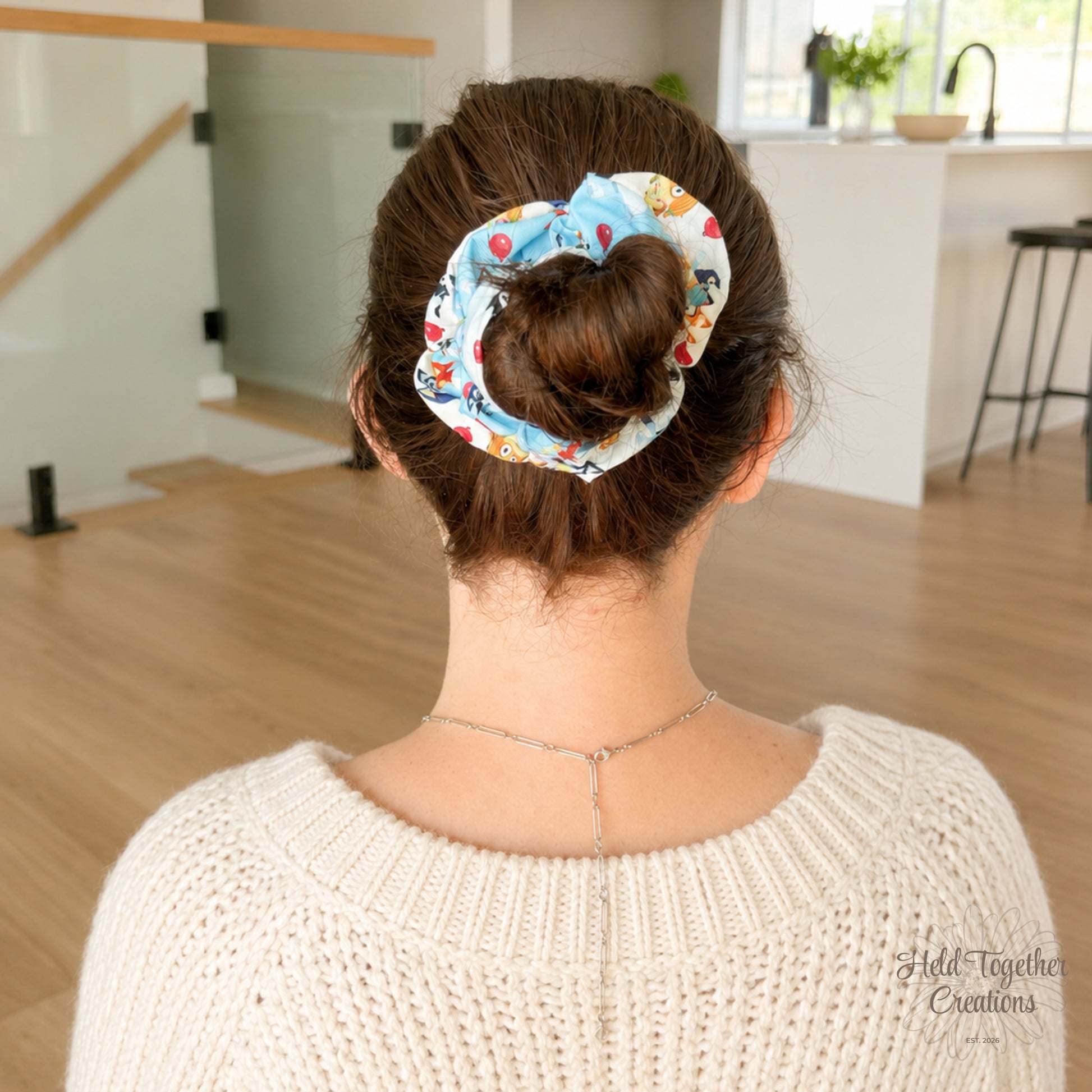 Balloon Bash scrunchie styled in a brown hair bun, showing the blue puppy-print fabric in a bright home setting.