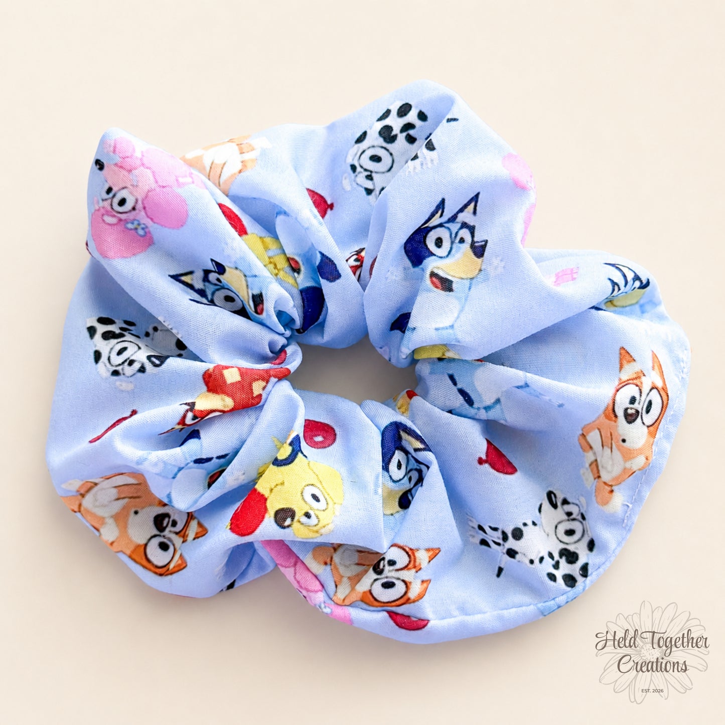 Balloon Pup handmade scrunchie in light blue puppy-print fabric on a warm ivory background with Held Together Creations branding.