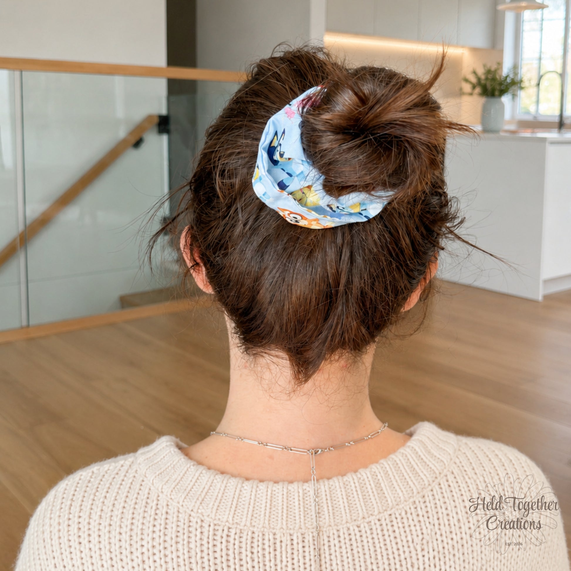 Balloon Pup scrunchie styled in a brown hair bun, showing the light blue puppy-print fabric in a soft home setting.