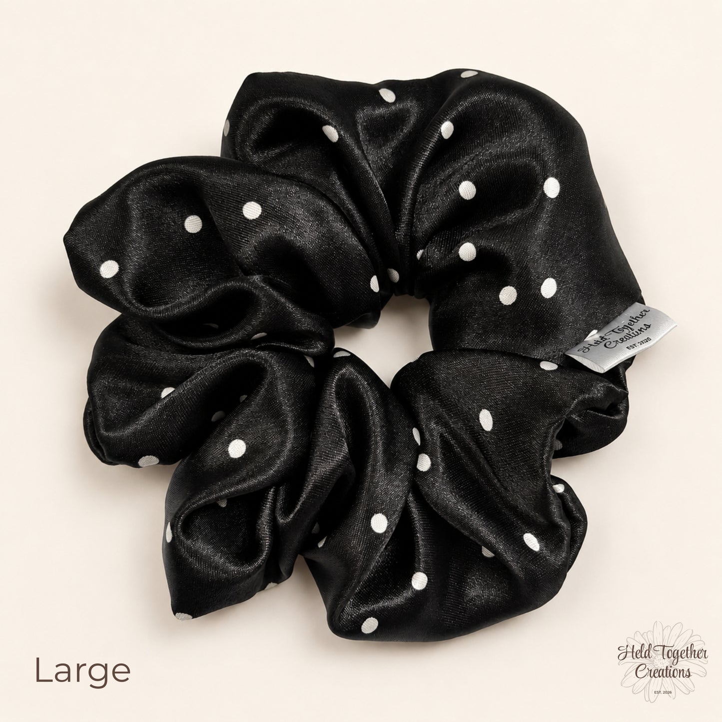Large black satin scrunchie with white spot pattern on a soft ivory background.