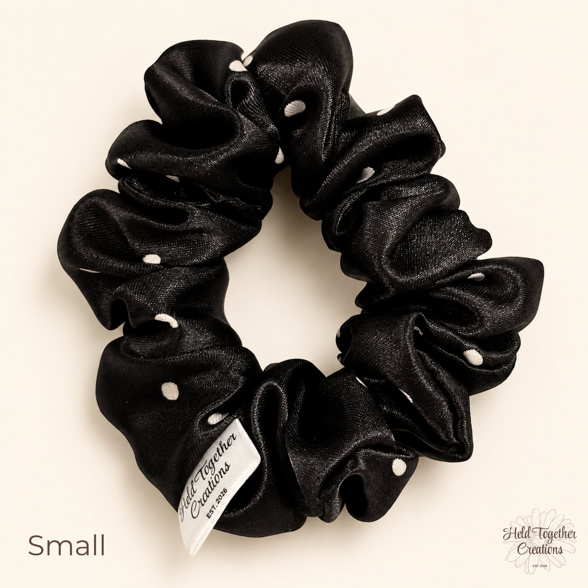 Small black satin scrunchie with white spot pattern on a soft ivory background.