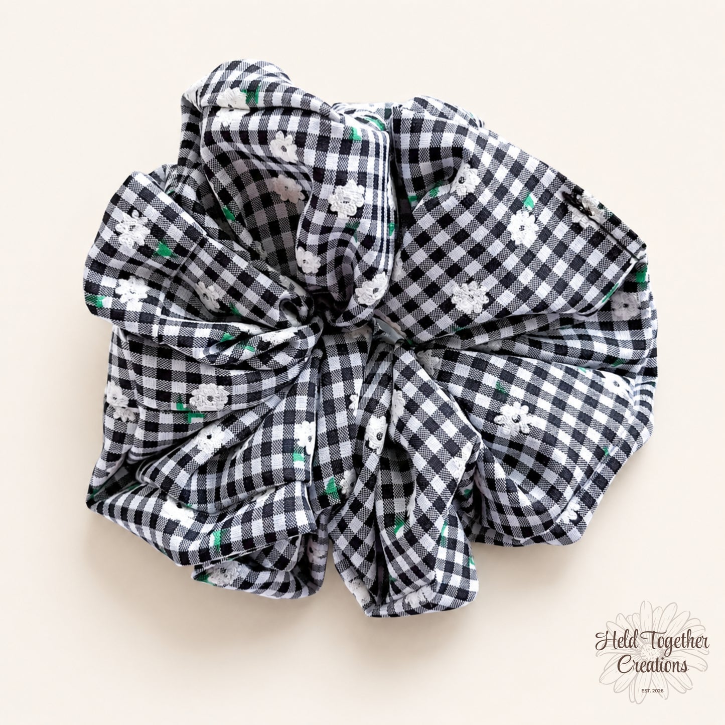 Black and white gingham floral fabric scrunchie displayed flat on a warm ivory background.