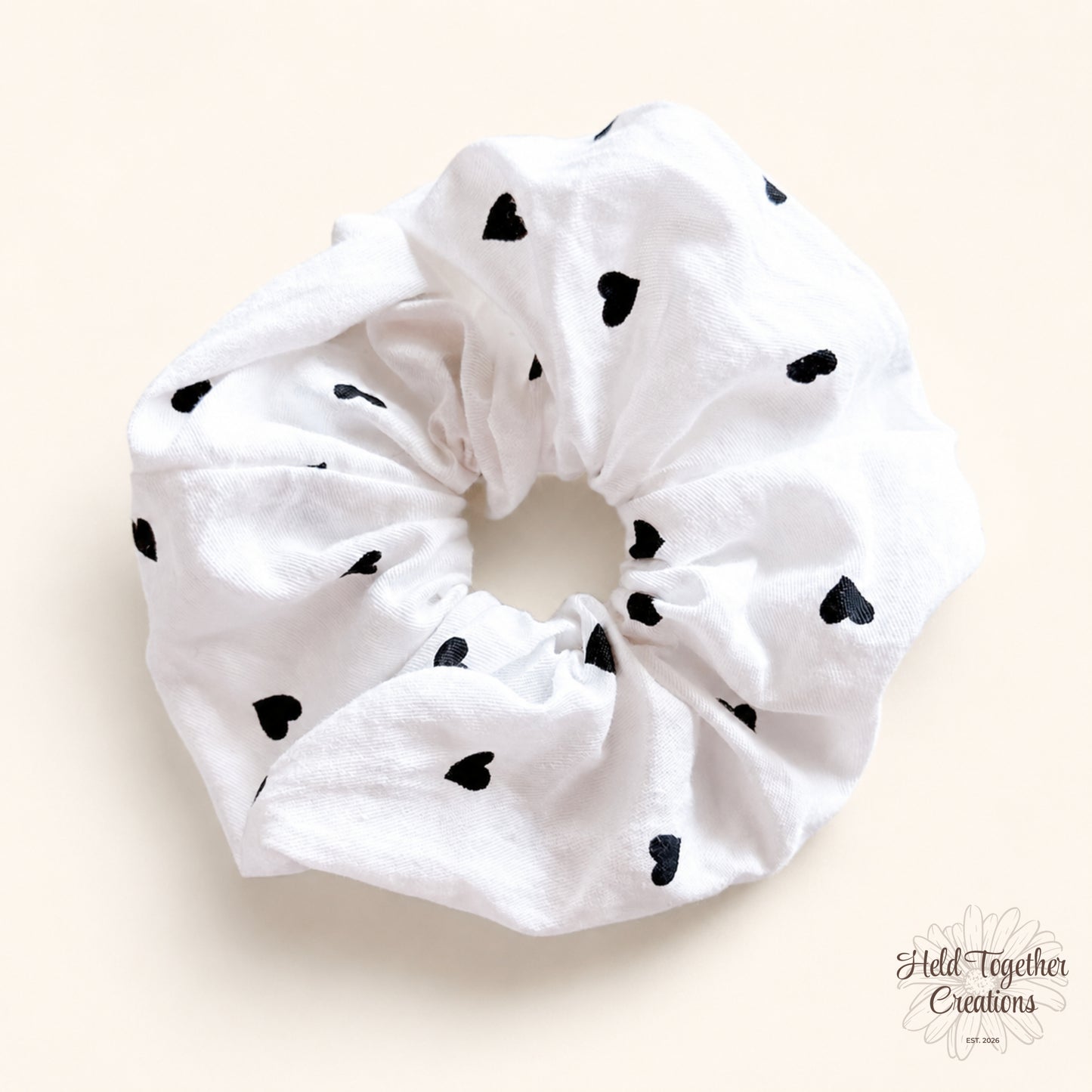White handmade fabric scrunchie with scattered black heart print on a soft neutral background.
