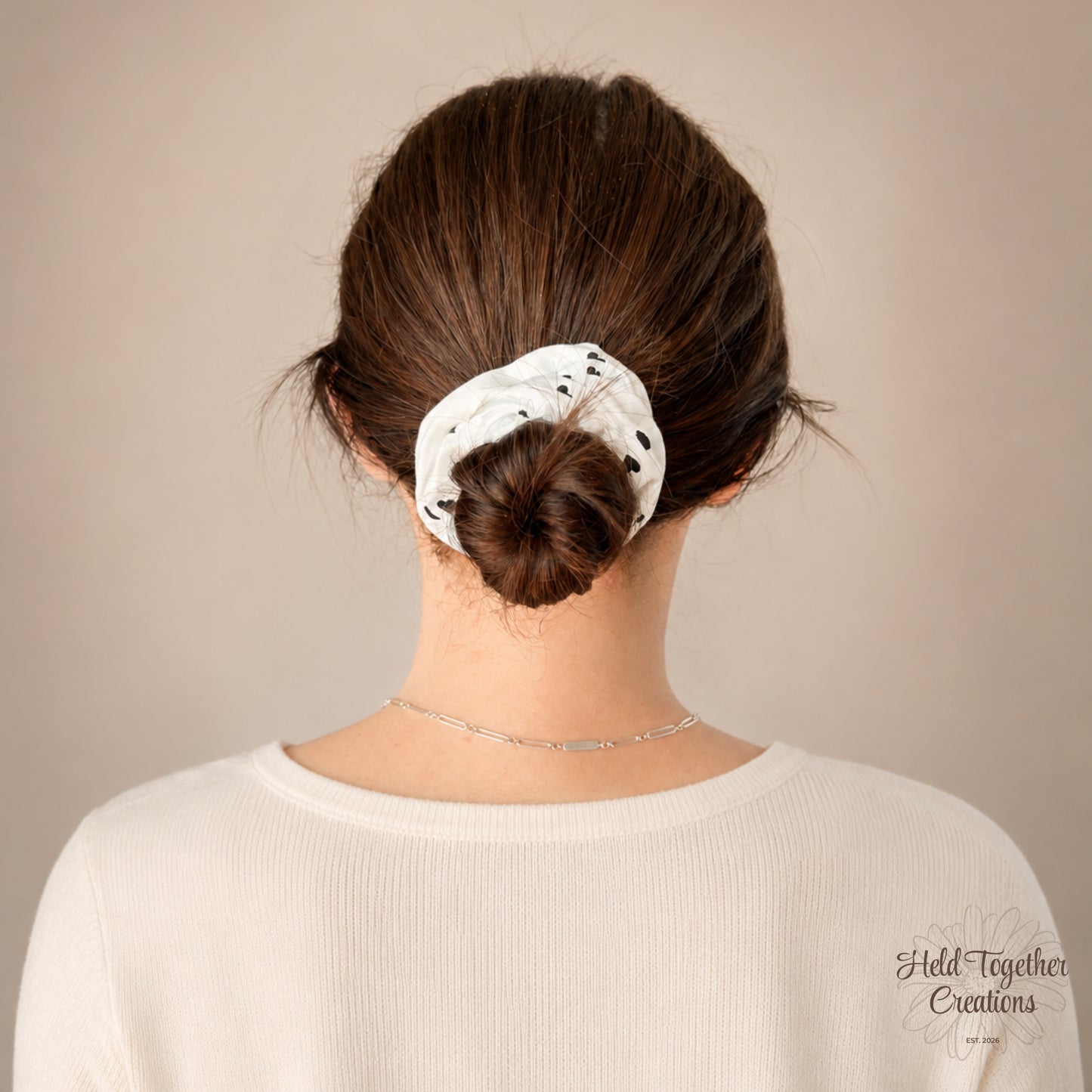 White handmade fabric scrunchie with scattered black heart print on a soft neutral background.