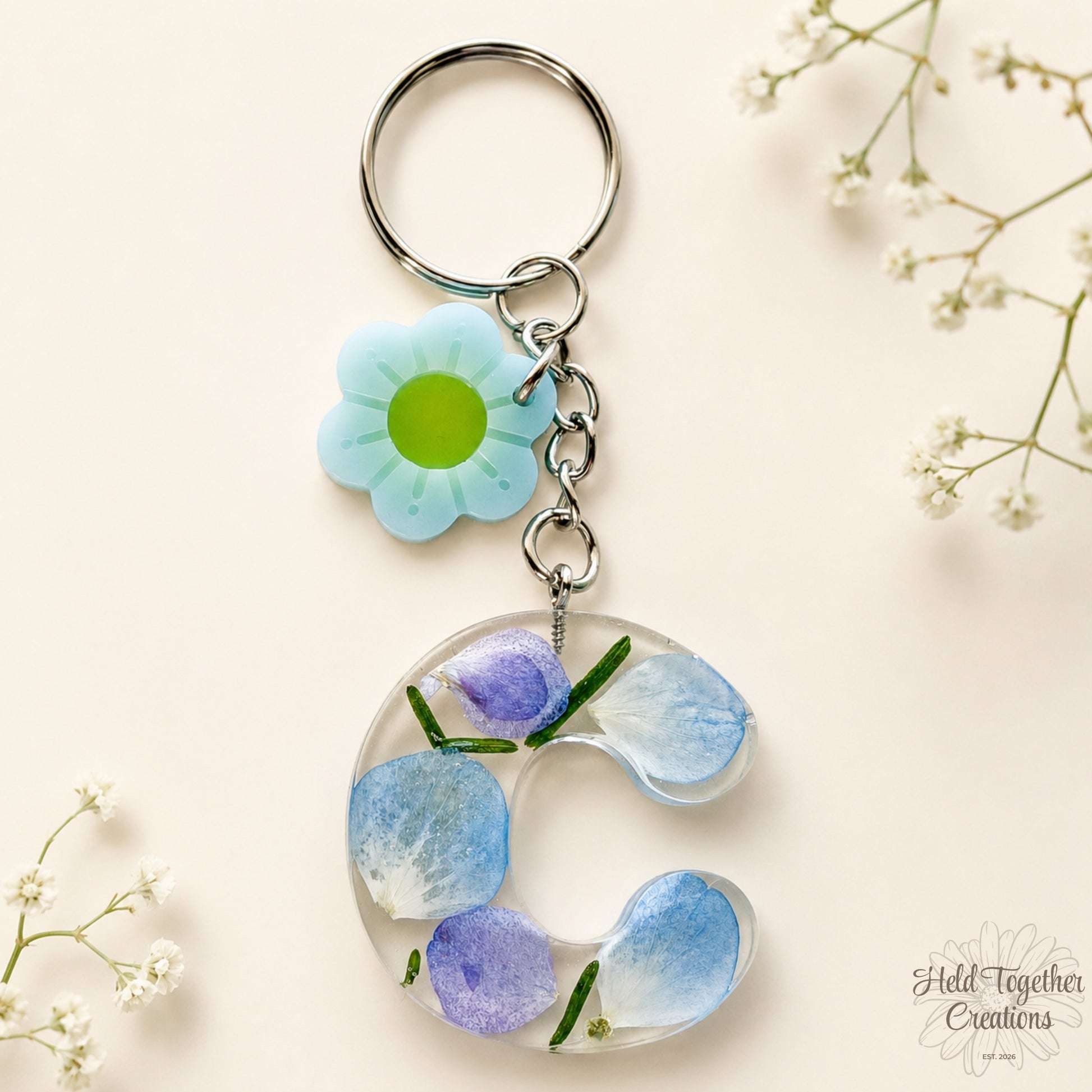 Handmade clear resin initial keyring with blue and purple floral details and a daisy charm on silver hardware.