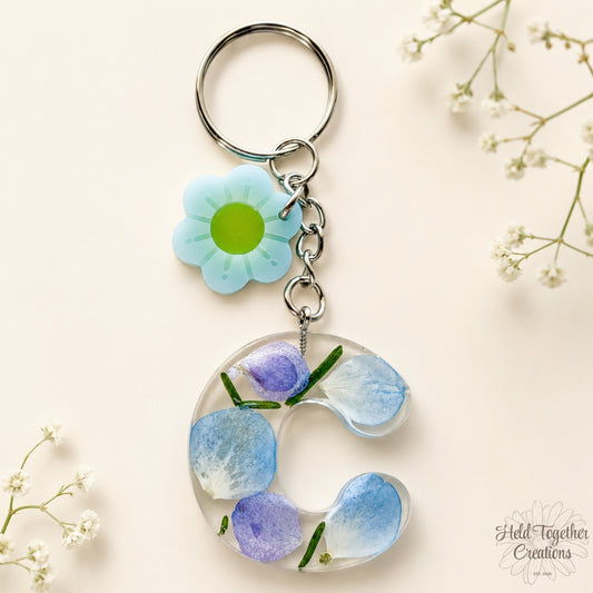 Handmade clear resin initial keyring with blue and purple floral details and a daisy charm on silver hardware.