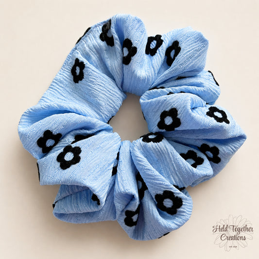 Blue Daisy Pop handmade scrunchie in textured light blue fabric with black daisy print.