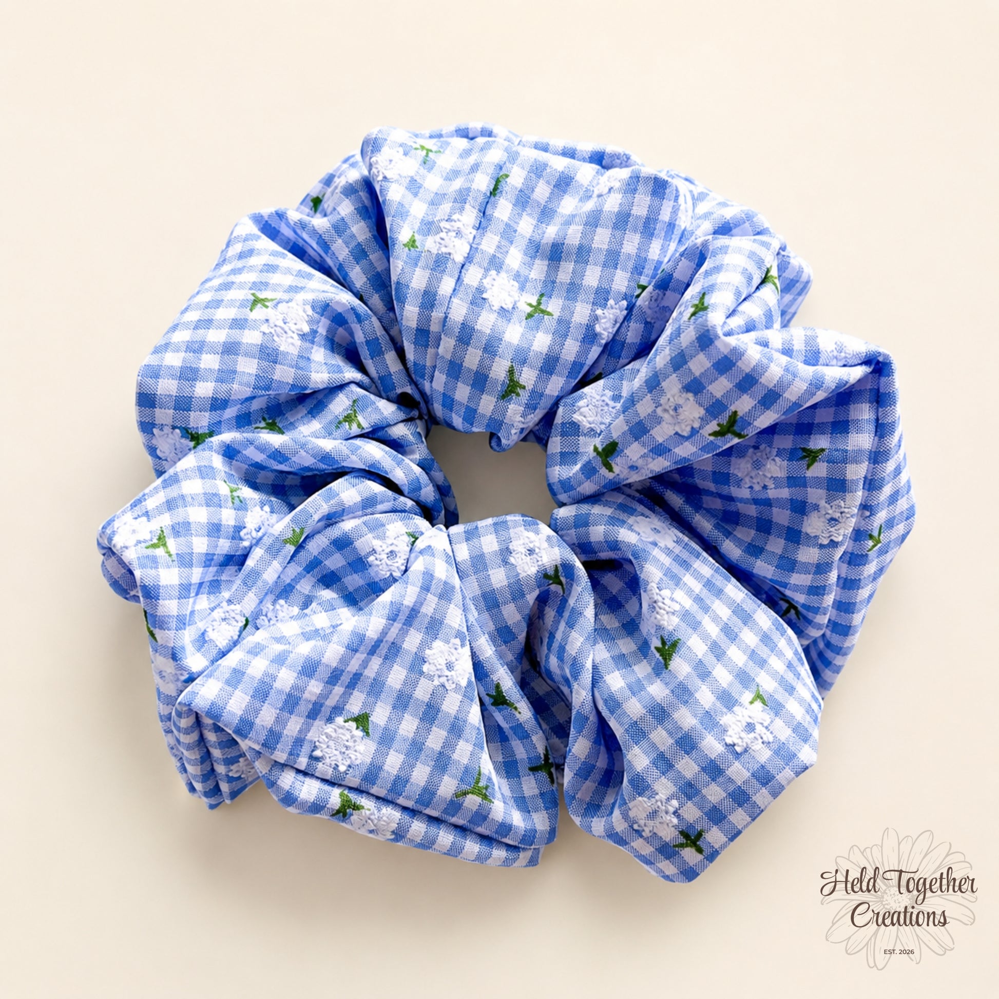 Blue and white gingham floral handmade scrunchie with soft gathered fabric on a warm neutral background.