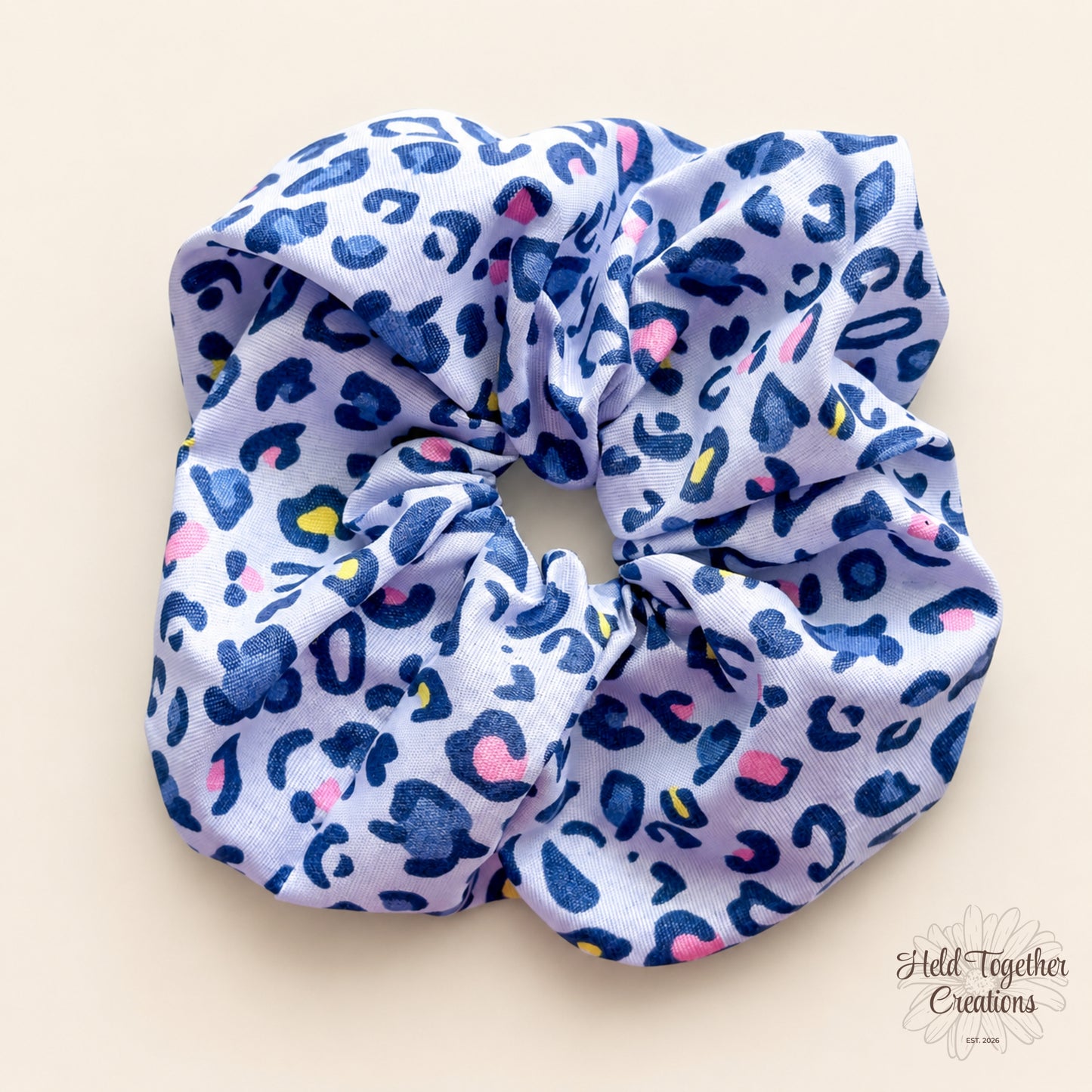 Blue Prowl handmade fabric scrunchie with a light blue base, navy leopard print pattern, and pink and yellow accent details.