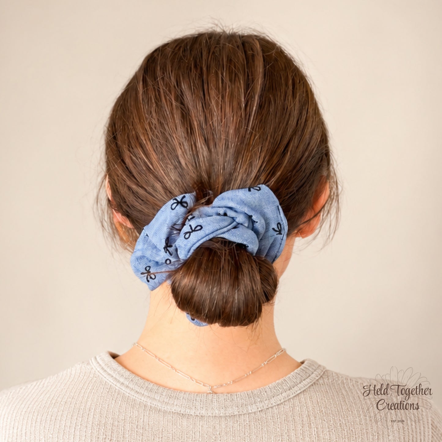 Blue handmade fabric scrunchie with black bow pattern on a warm ivory background.
