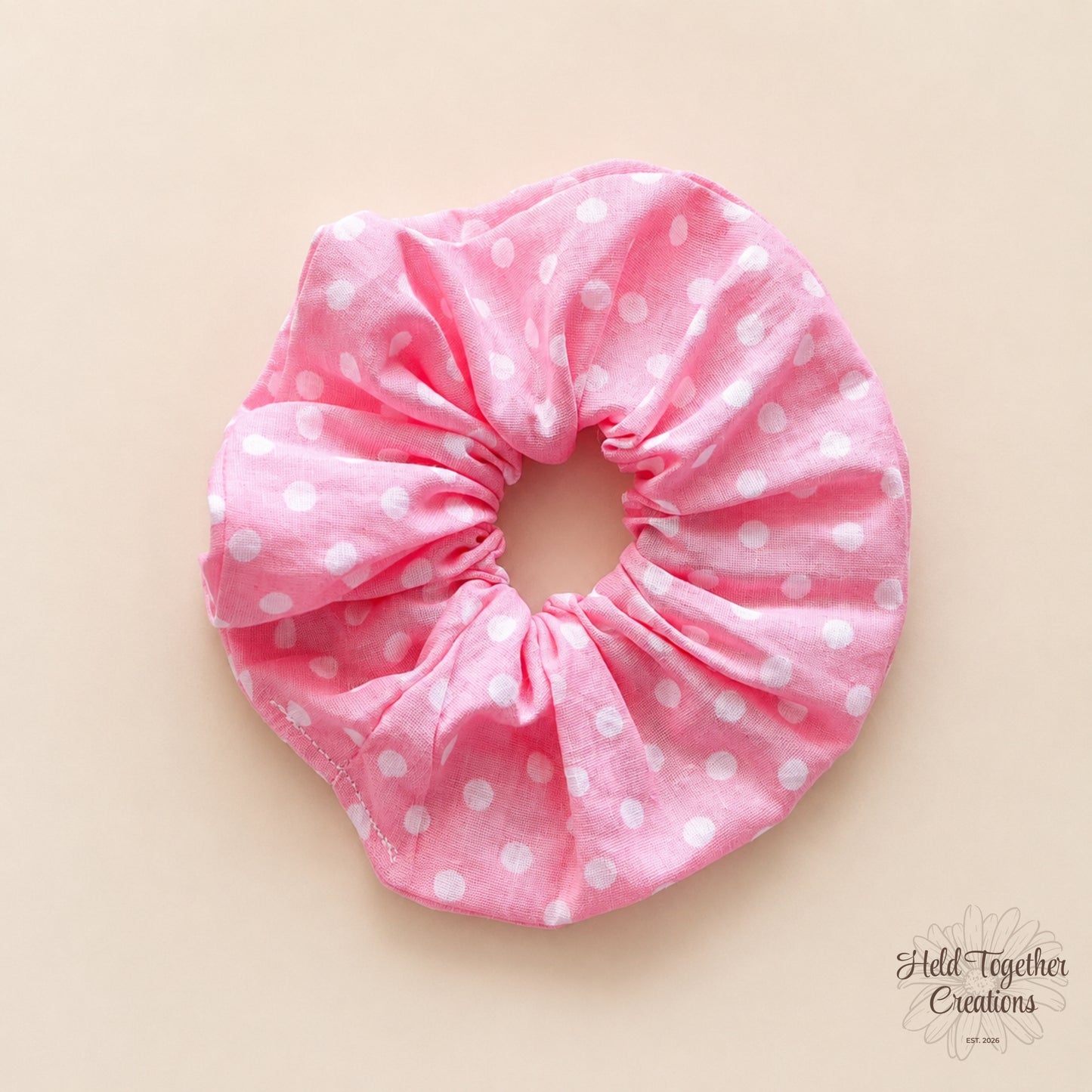 Pink scrunchie with white polka dots on a beige background