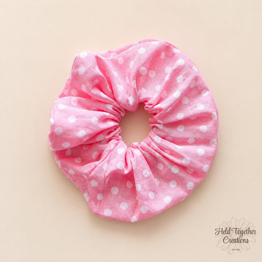 Pink scrunchie with white polka dots on a beige background