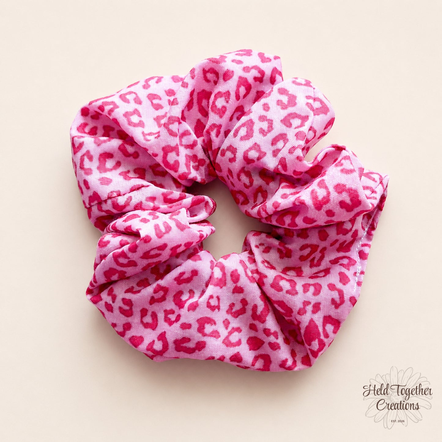 Pink leopard print handmade fabric scrunchie on a warm ivory background.