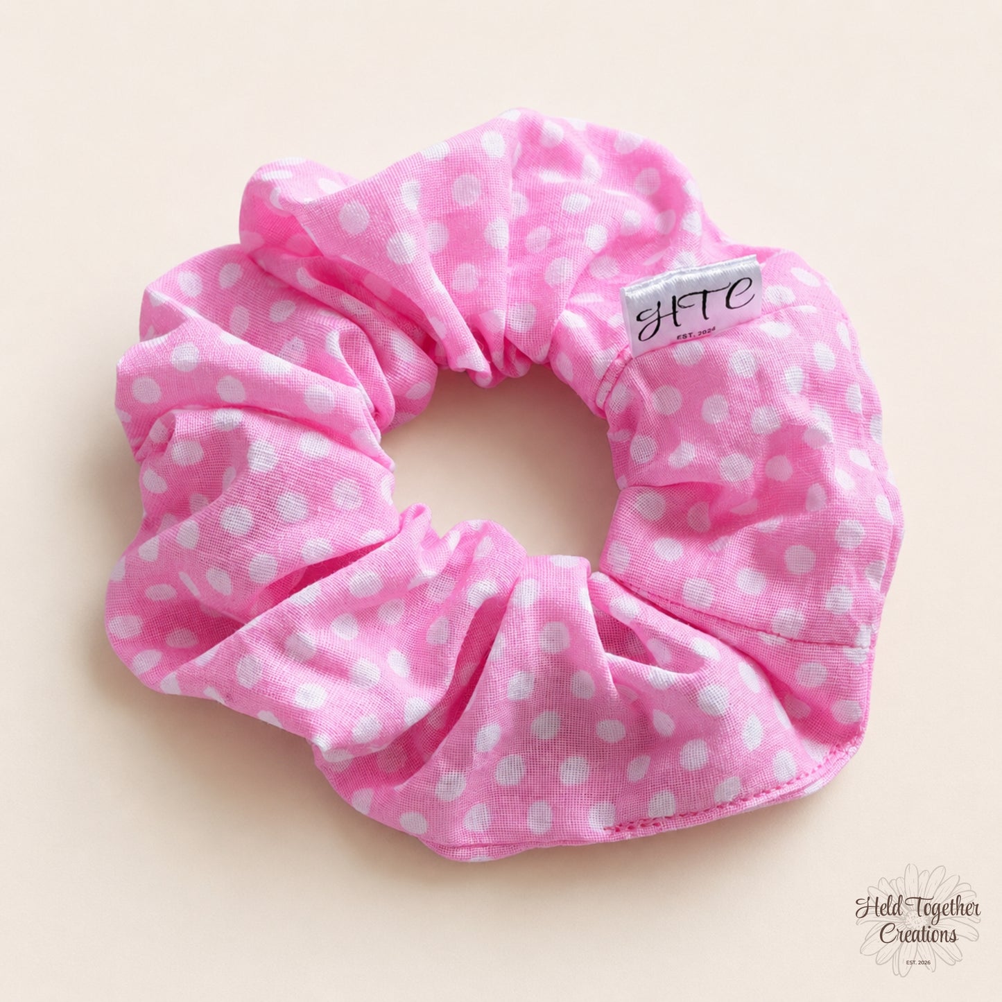 Pink handmade scrunchie with white polka dots on a warm neutral background.